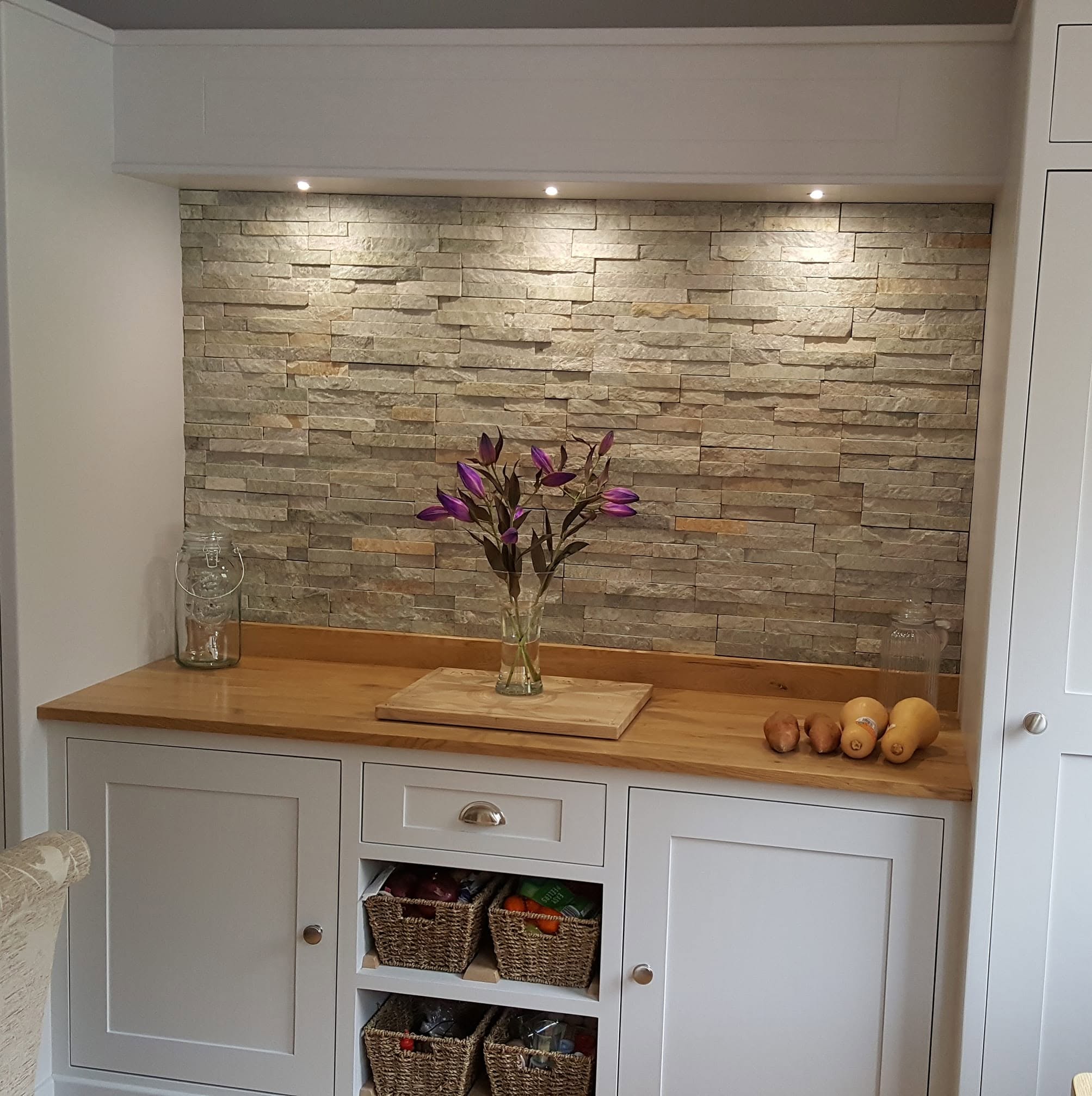 Textured feature alcove above painted cabinets and a wooden worktop