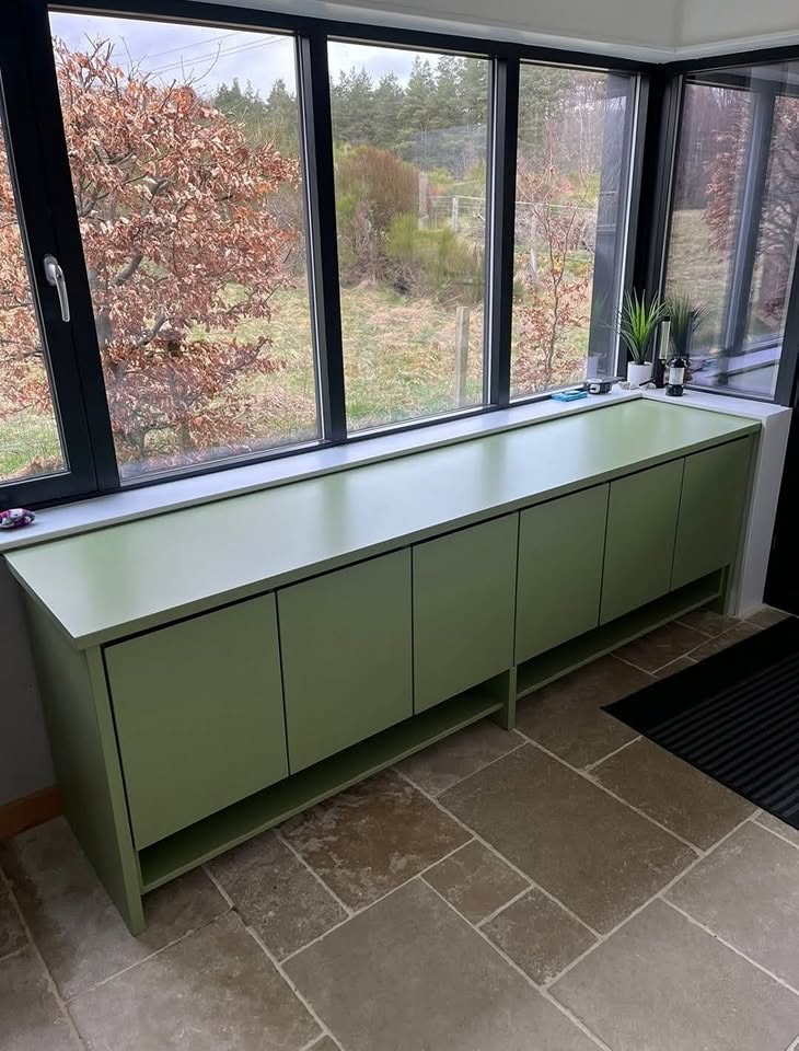 Green painted cabinetry beneath large windows